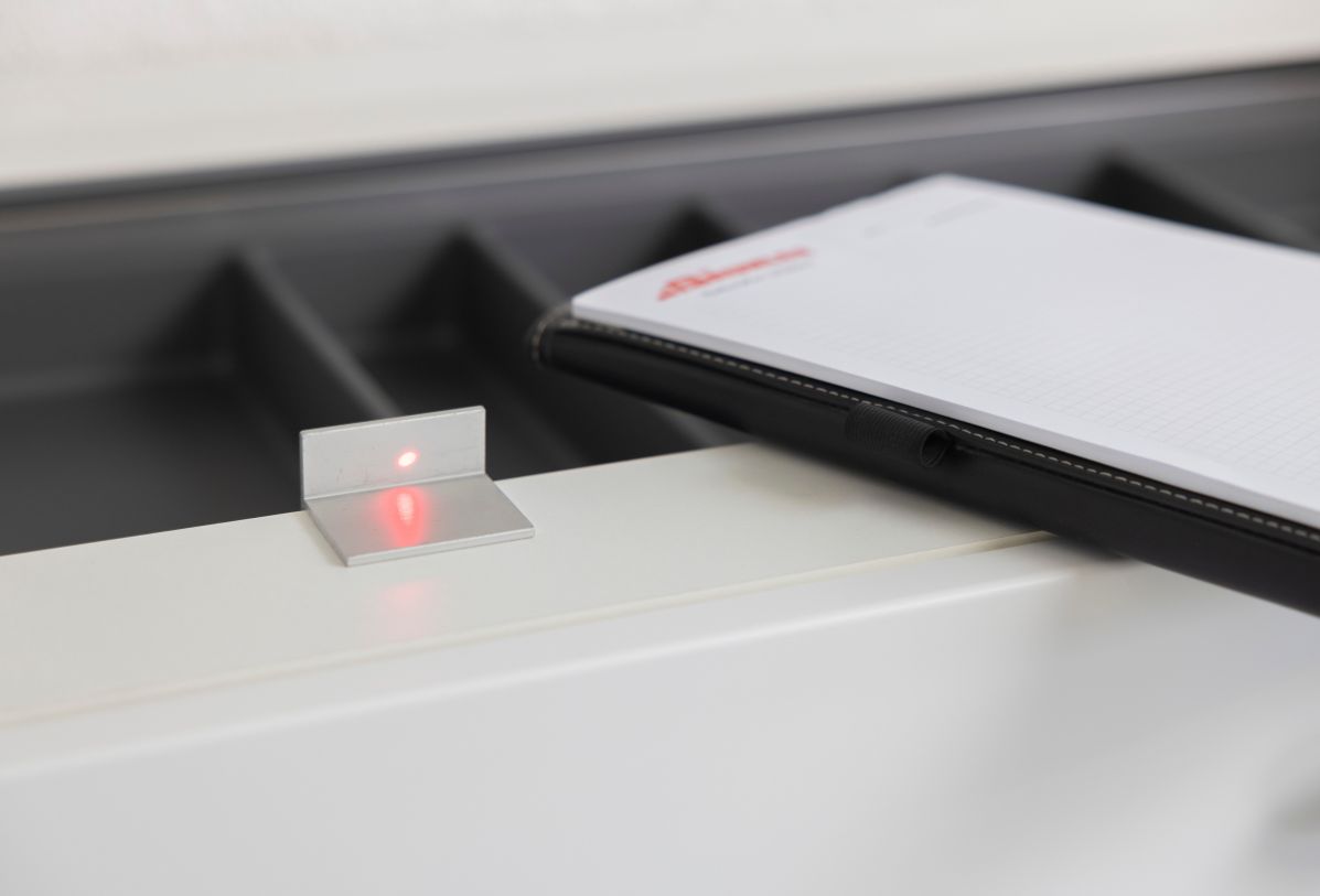 Roter Laser-Punkt auf einem Küchenkorpus zu sehen, um das Aufmaß einer Küchenarbeitsplatte zu nehmen. Im Hintergrund ein karierter Block und eine Aktenmappe
