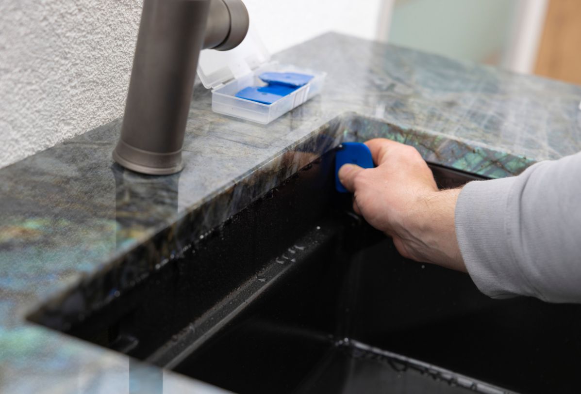 Das Spülbecken einer Küche wird silikoniert, nachdem die Küchenarbeitsplatte aus Naturstein gesetzt wurde.