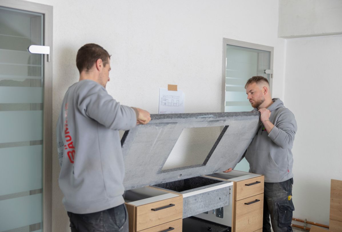 Zwei Produktionsarbeiter sind dabei, eine Küchenarbeitsplatte aus Naturstein zu setzen.